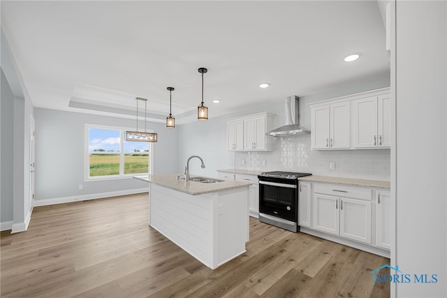 kitchen with sink, an island with sink, white cabinetry, wall chimney range hood, and stainless steel range