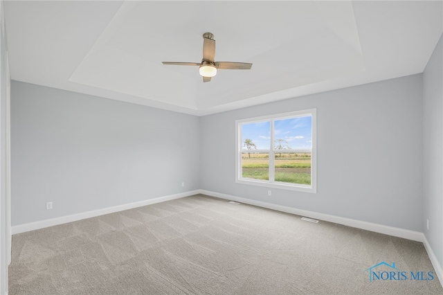 carpeted spare room featuring ceiling fan and a raised ceiling