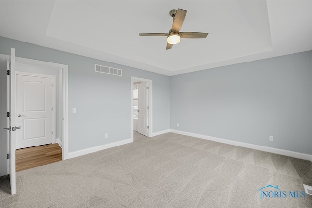 unfurnished bedroom with a tray ceiling, ceiling fan, and light colored carpet