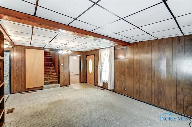 basement featuring light colored carpet, a drop ceiling, and wooden walls