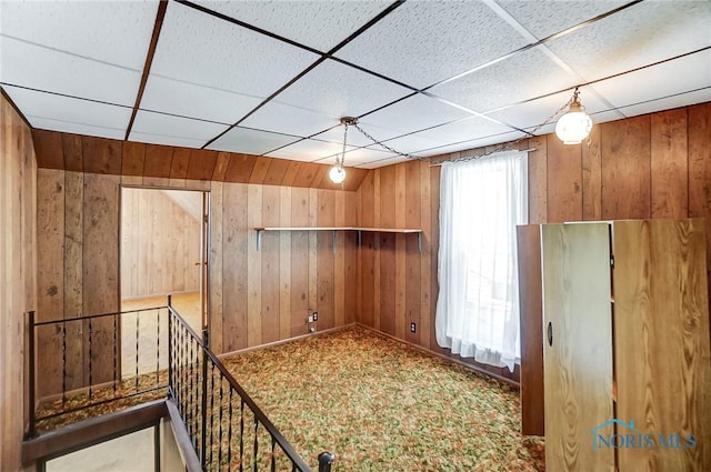 unfurnished room featuring lofted ceiling, a drop ceiling, carpet, and wooden walls