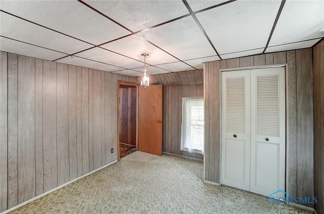 interior space featuring light colored carpet, a closet, a drop ceiling, and wood walls