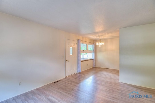 unfurnished room with light wood-type flooring and a chandelier