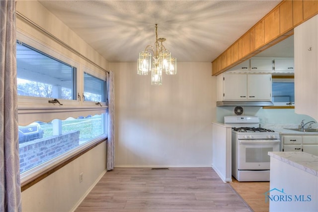 kitchen with white cabinetry, white range with gas stovetop, hanging light fixtures, a chandelier, and sink