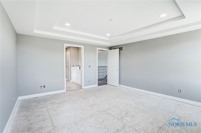 unfurnished bedroom with a tray ceiling and ensuite bath