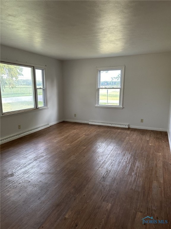 spare room with a baseboard radiator, a wealth of natural light, and dark hardwood / wood-style flooring