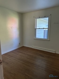 empty room with dark wood-type flooring and a baseboard radiator