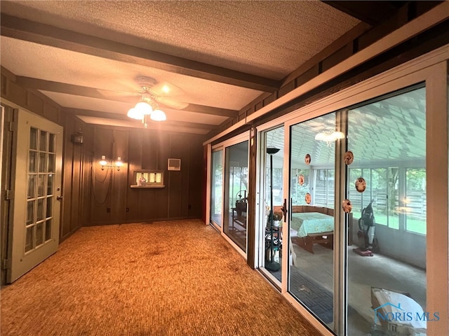 interior space featuring wood walls, a textured ceiling, beamed ceiling, ceiling fan, and carpet