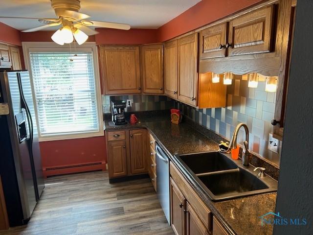 kitchen with sink, appliances with stainless steel finishes, wood-type flooring, decorative backsplash, and a baseboard radiator