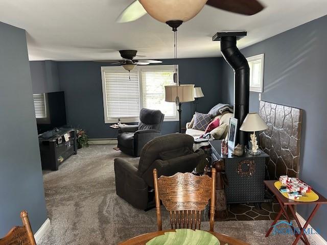 living room with baseboard heating, ceiling fan, carpet flooring, and a wood stove