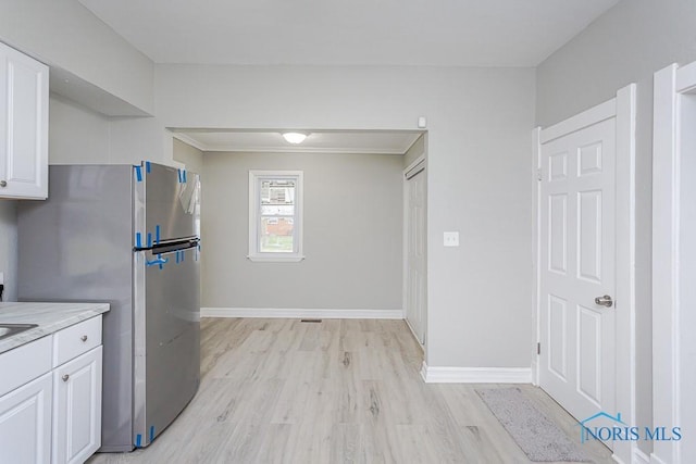 kitchen featuring light wood-type flooring, white cabinetry, crown molding, and stainless steel refrigerator