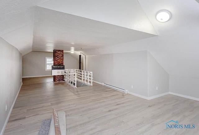 additional living space featuring light wood-type flooring, vaulted ceiling, and a baseboard heating unit