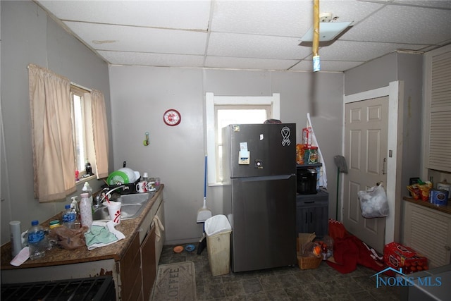 kitchen featuring dark tile patterned flooring, a drop ceiling, black fridge, and sink