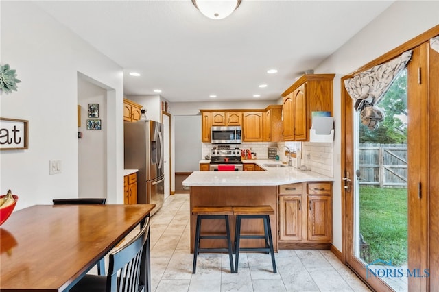 kitchen with a breakfast bar area, stainless steel appliances, sink, kitchen peninsula, and decorative backsplash