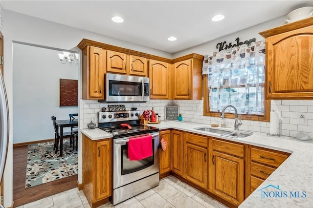 kitchen with light wood-type flooring, stainless steel appliances, a chandelier, sink, and decorative backsplash