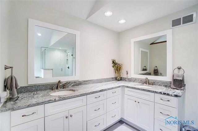 bathroom with a shower with shower door and double sink vanity