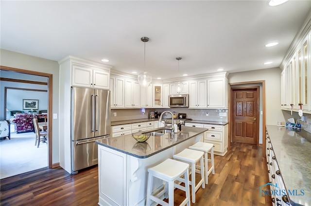 kitchen featuring dark carpet, white cabinets, a kitchen island with sink, stainless steel appliances, and decorative light fixtures