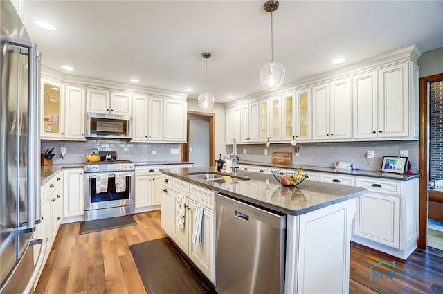 kitchen with white cabinetry, backsplash, a kitchen island with sink, stainless steel appliances, and hardwood / wood-style floors