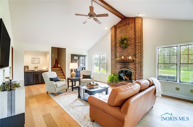 living room featuring a fireplace, ceiling fan, light wood-type flooring, brick wall, and beam ceiling