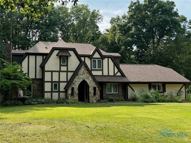 tudor house with a shingled roof, a front yard, and stucco siding