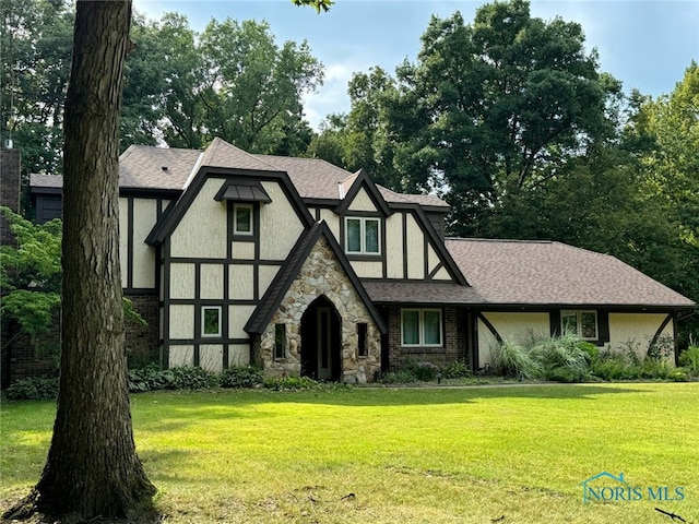 tudor-style house with a shingled roof, a front lawn, and stucco siding