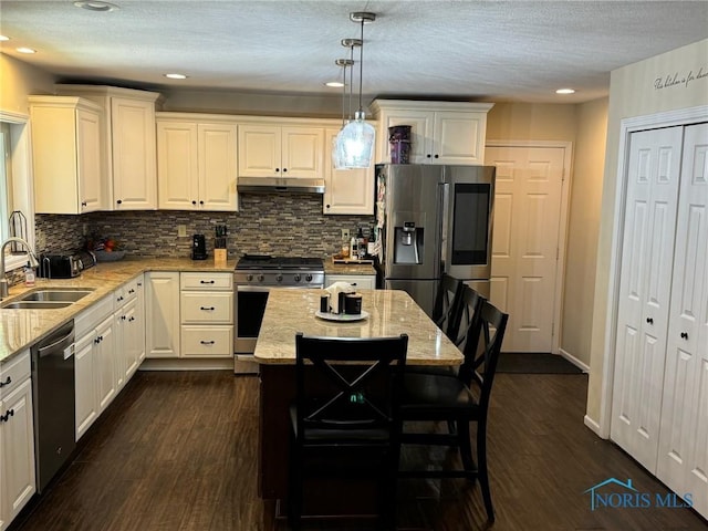 kitchen with appliances with stainless steel finishes, a center island, light stone countertops, pendant lighting, and a sink