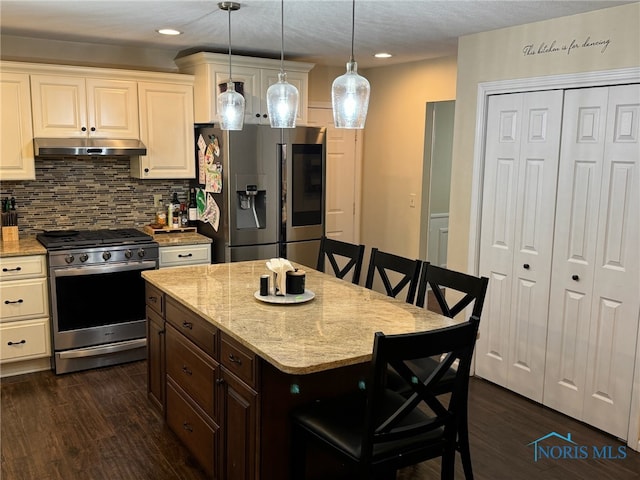 kitchen with appliances with stainless steel finishes, a breakfast bar, pendant lighting, dark hardwood / wood-style flooring, and a center island