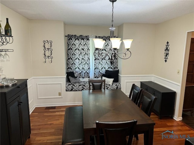 dining room featuring a wainscoted wall, dark wood-style flooring, an inviting chandelier, and a decorative wall