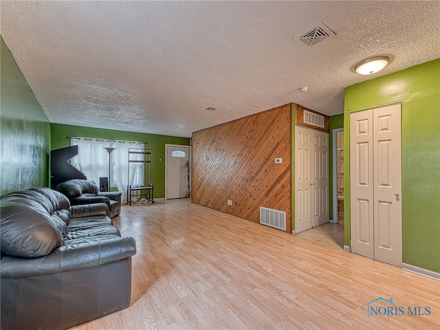 living room featuring wood walls, light hardwood / wood-style floors, and a textured ceiling