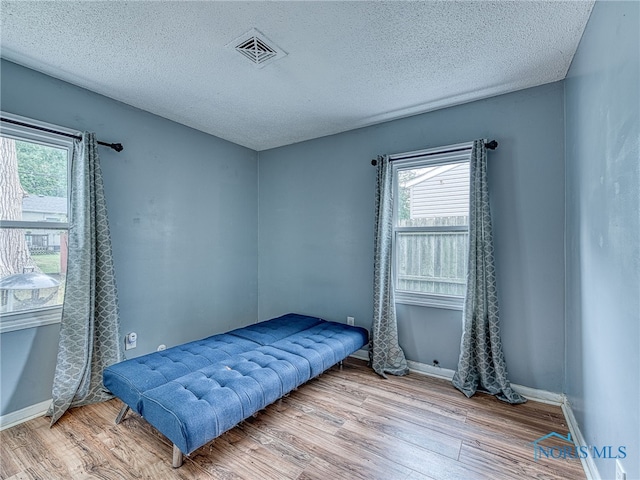 bedroom with a textured ceiling, light wood-type flooring, and multiple windows