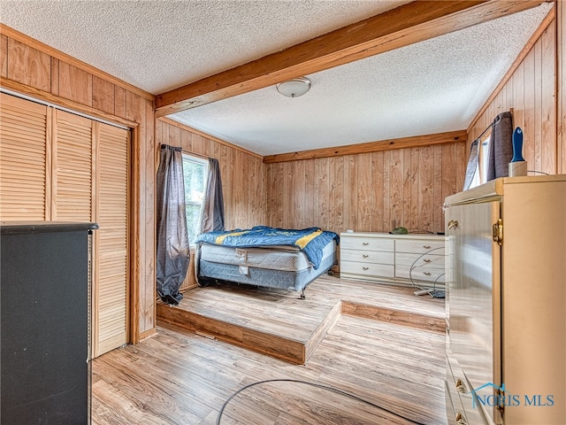 bedroom featuring a textured ceiling, wood walls, light hardwood / wood-style flooring, a closet, and beam ceiling