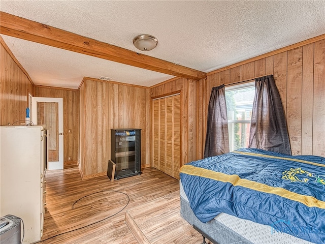 bedroom featuring a textured ceiling, light hardwood / wood-style flooring, wood walls, a closet, and beam ceiling