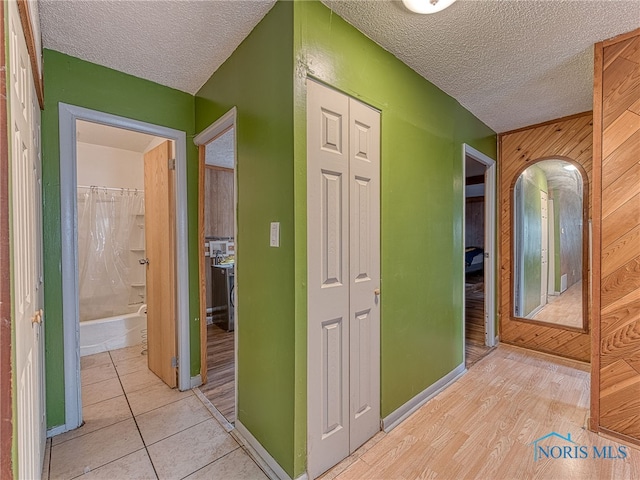 corridor with a textured ceiling, wood walls, and light hardwood / wood-style floors