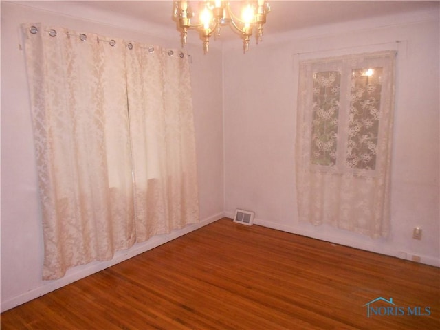 empty room with hardwood / wood-style flooring and a chandelier