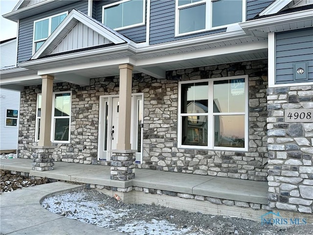 doorway to property featuring stone siding, a porch, and board and batten siding