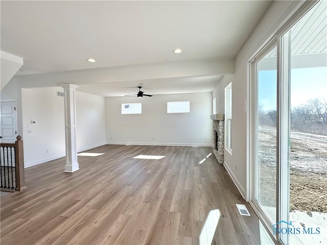 interior space featuring light wood-type flooring, decorative columns, a fireplace, and visible vents