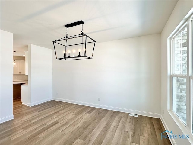 unfurnished room featuring light wood-type flooring, visible vents, baseboards, and an inviting chandelier