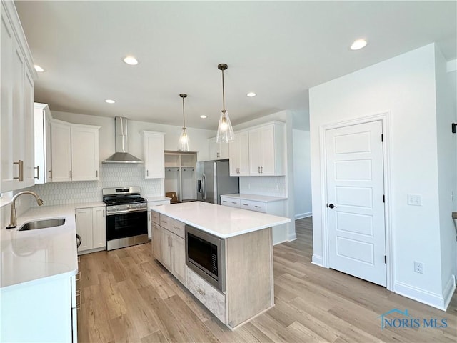 kitchen with white cabinets, wall chimney exhaust hood, a center island, stainless steel appliances, and a sink