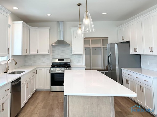 kitchen featuring appliances with stainless steel finishes, white cabinetry, a sink, a kitchen island, and wall chimney exhaust hood