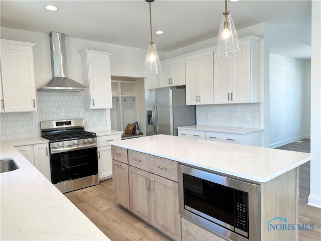 kitchen featuring wall chimney exhaust hood, light stone counters, white cabinetry, and stainless steel appliances