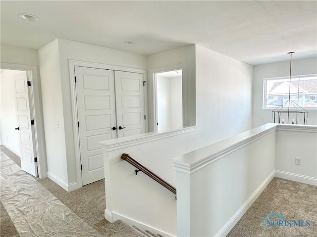 hallway with light carpet, an upstairs landing, and baseboards