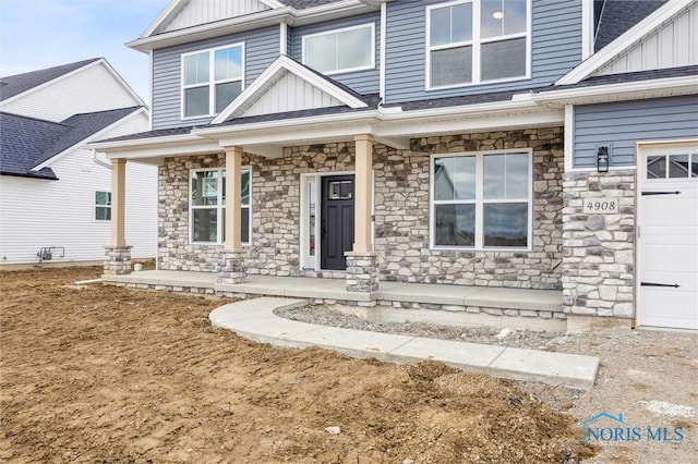 view of front facade with stone siding, covered porch, board and batten siding, and an attached garage