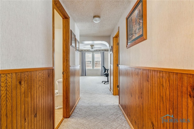 corridor with light carpet, wooden walls, and a textured ceiling