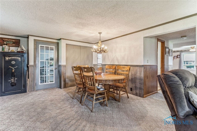 carpeted dining space featuring plenty of natural light, a chandelier, a textured ceiling, and wood walls