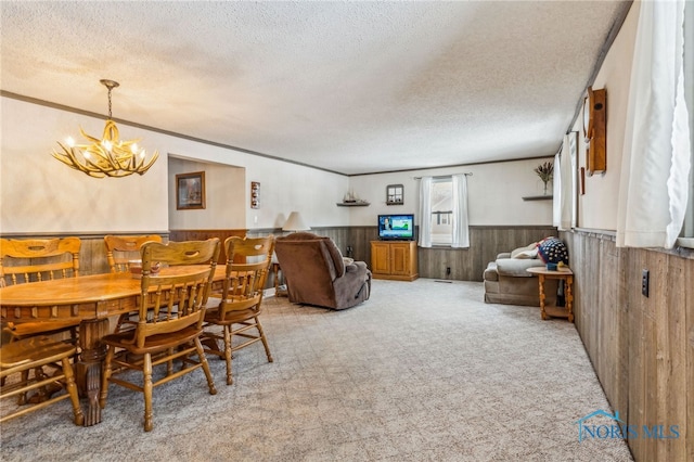 dining space with light carpet, an inviting chandelier, a textured ceiling, and wood walls