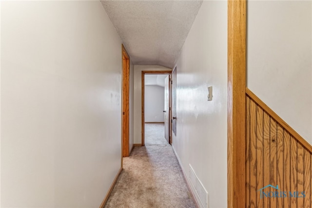 hall with vaulted ceiling, light carpet, and a textured ceiling