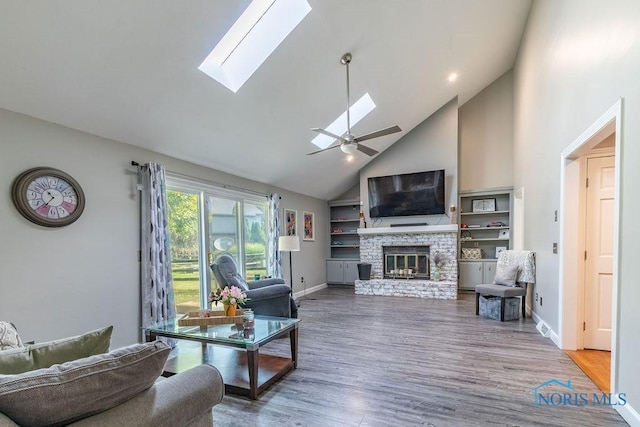 living area with a skylight, a fireplace, ceiling fan, wood finished floors, and baseboards