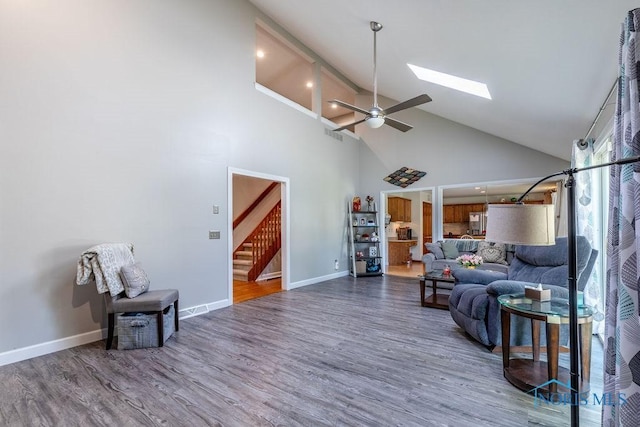 living room featuring a skylight, stairway, wood finished floors, high vaulted ceiling, and baseboards