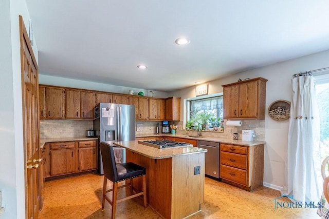 kitchen with brown cabinets, a center island, stainless steel appliances, light countertops, and a sink