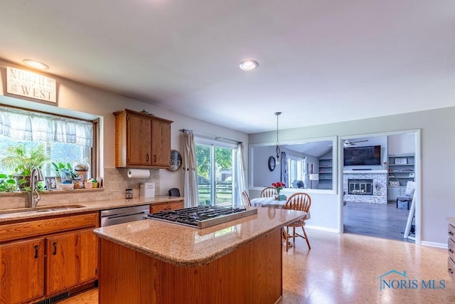 kitchen with stainless steel appliances, a kitchen island, a sink, brown cabinetry, and a glass covered fireplace